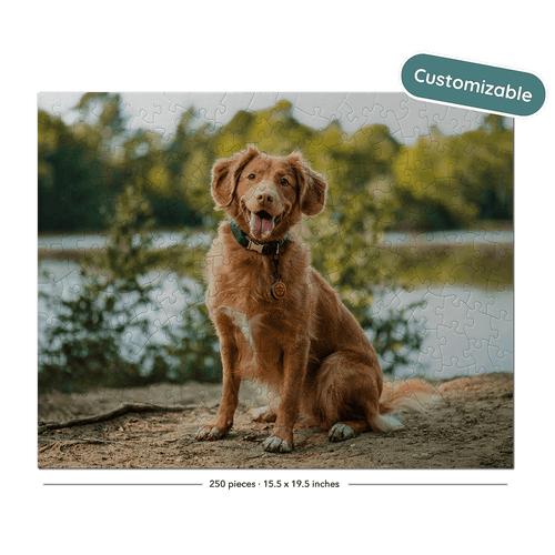 A custom jigsaw puzzle featuring a golden retriever dog sitting on a sandy shore with a lake and trees in the background. The puzzle is displayed on a black background with a 'Customizable' badge in the top right and a piece count label at the bottom.