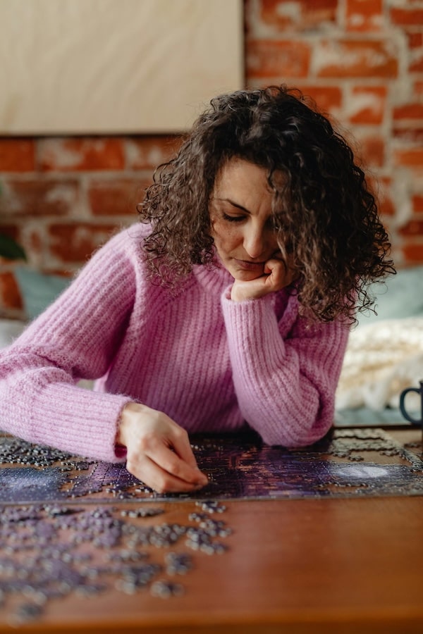 Woman in a pink sweater working on a puzzle with a brick wall background